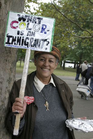Stan Schnier, A woman at the Immigrant Workers Freedom Ride holds a sign that asks “What color is an immigrant?”, Flushing Meadows Corona Park, New York, New York, October 4, 2003.   Stan Schnier, A woman at the Immigrant Workers Freedom Ride holds a sign that asks “What color is an immigrant?”, Flushing Meadows Corona Park, New York, New York, October 4, 2003.