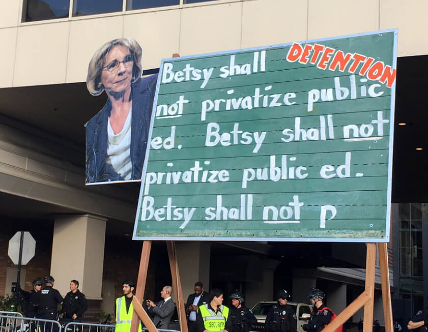 Sign protesting Betsy DeVos at a rally, Bellevue, Washington, October 13, 2017. Photograph by Flickr user Backbone Campaign. Creative Commons license CC BY 2.0. Sign protesting Betsy DeVos at a rally
