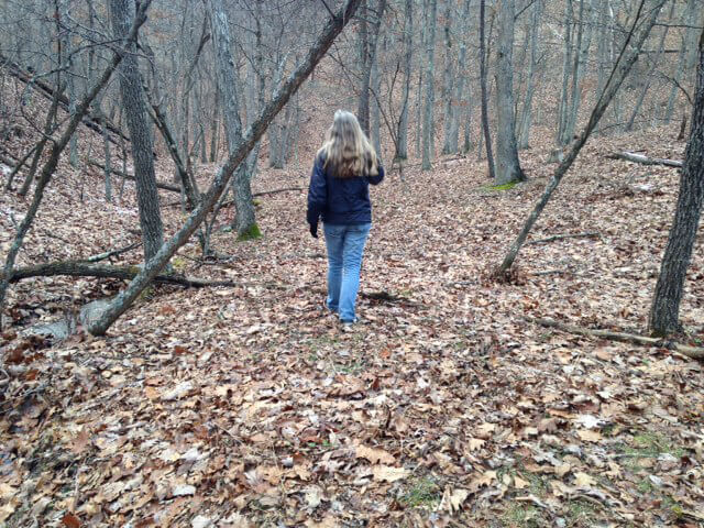 Me Up the Hollow, Romney, West Virginia, December 14, year unknown. Photograph by Ann Pancake. Courtesy of Ann Pancake. Photograph of Ann Pancake in the woods in winter, walking away from the camera.