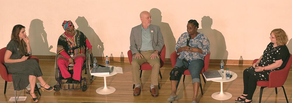 Quilting Conversation panelists, Atlanta, Georgia, September 22, 2018. From left: Katherine Jentleson, Marquetta Johnson, Michael Moon, Mary Margaret Pettway, and Erin Jane Nelson. Screenshot courtesy of Southern Spaces. A photograph of four women and one man sitting on a stage in front of a white backdrop. One of the women speaks into a microphone; the others are turned towards her, listening.
