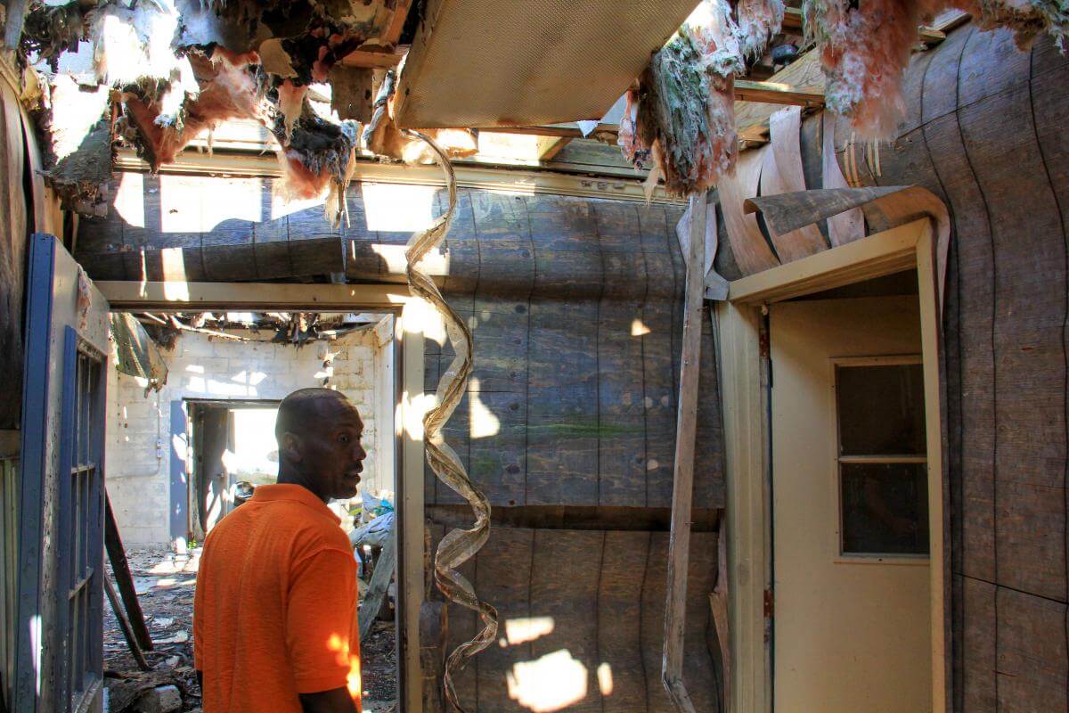 Tour of the ruins of Ed Scott's catfish processing plant with Daniel Scott, Leflore County, Mississippi, 2013. Photograph by Julian Rankin. © Julian Rankin. Daniel Scott standing in a ruined building with holes in the ceiling, exposed insulation, and littered floor, looking back toward the camera