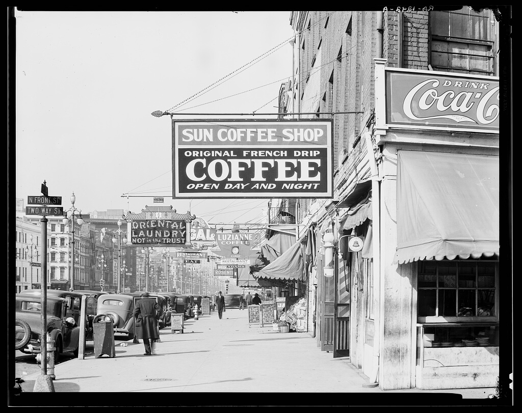 New Orleans downtown street, Louisiana, 1935. Photograph by Walker Evans. Courtesy of Library of Congress Prints and Photographs Division, Washington, DC, loc.gov/pictures/item/2017759415. Black and white image of a New Orleans downtown street, showing a coffee shop with a sign reading, "Sun Coffee Shop, Original Drench Drip Coffee, Open Day and Night"