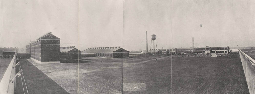 Kilby Prison - General Inside View, Montgomery, Alabama, ca. 1919. Photograph by unknown creator. Originally published in the quadrennial report of the Board of Control and Economy of the Alabama State Board of Administration for the years 1919 to 1922. Courtesy of Alabama Department of Archives and History. A wide view, black and white photograph showing a prison yard, brick prison buildings, and water tower inside tall fences.