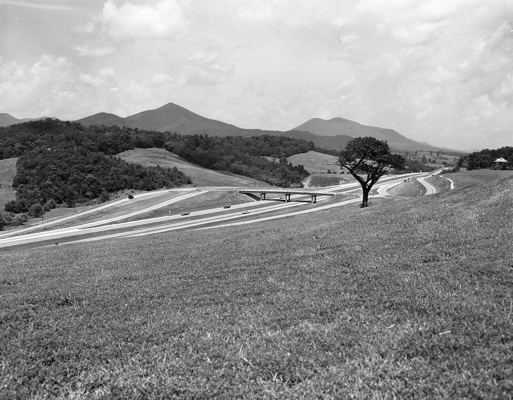 Black and white photograph of an interstate with rolling mountains in the background.