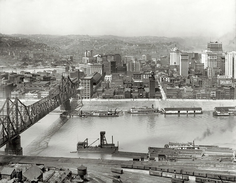 Black and white photograph of Wabash Bridge, showing boats and liners on the river in a circa 1908 industrial cityscape.
