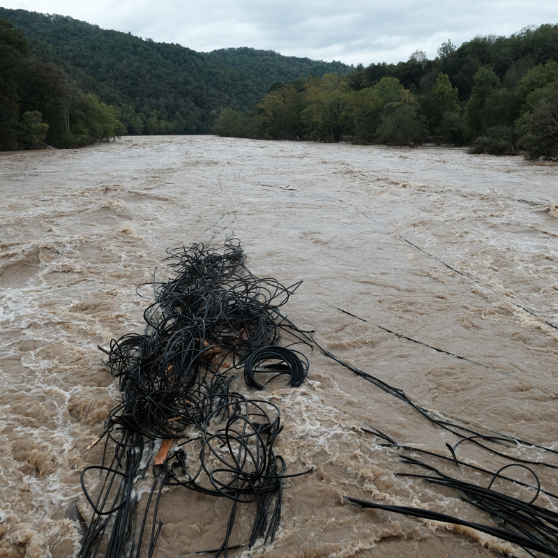 Raging French Broad River at flood stage during Hurricane Helene near Marshall, North Carolina with mass of black PVC pipe tangled in bridge piling.